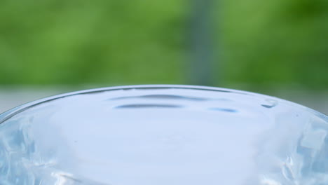 A-single-drop-of-water-hitting-the-surface-of-crystal-clear-water-causing-movement-and-wave-in-a-transparent-glass-cup-on-a-blurry-background