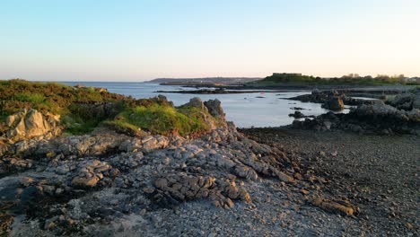 Low-flight-over-rocky-beach-and-foreshore-Bordeaux-Guernsey-at-low-tide-with-calm-sea-on-bright-late-afternoon