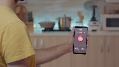 Mann-Hält-Handy-Mit-Lichtsteuerungs-App-In-Der-Küche-Und-Sitzt-In-Der-Küche