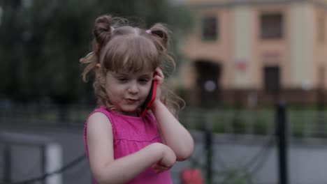 Child-girl-talking-by-smartphone-outdoors.-Kid-in-pink-dress-talking-by-mobile-phone-on-city-street