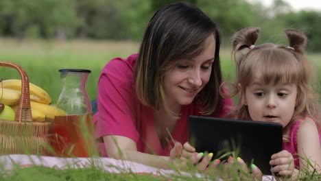 Family-weekend-picnic.-Daughter-child-girl-with-mother-play-online-games-on-tablet.-Chatting