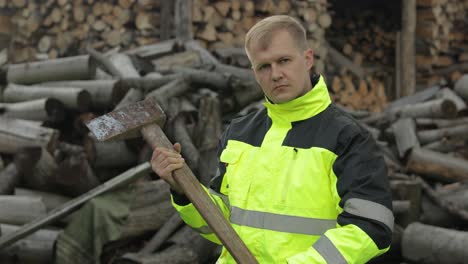 Lumberjack-in-reflective-jacket.-Man-woodcutter-with-big-axe.-Sawn-logs,-firewood-background