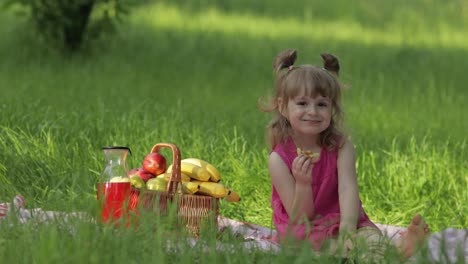 Weekend-at-picnic.-Caucasian-child-girl-on-grass-meadow-with-basket-full-of-fruits.-Eating-pancakes