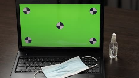 Hand-takes-mask-from-laptop-with-green-screen,-chroma-key.-Coronavirus-covid-19