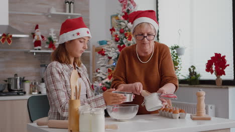 Senior-woman-putting-flour-in-metalic-siev-while-granddaughter-sift-ingredient-in-bowl