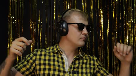 Portrait-of-caucasian-man-dancing-on-black-background.-Gold-shining-foil-strips.-Party,-music,-disco