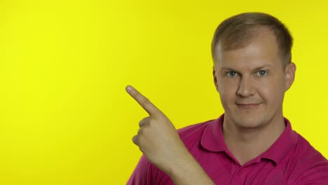 Portrait-of-young-man-posing-in-pink-t-shirt.-Happy-smiling-guy-pointing-at-something-with-hand