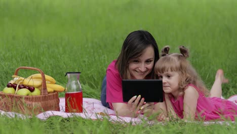 Family-weekend-picnic.-Daughter-child-girl-with-mother-study-lessons-on-tablet.-Distance-education