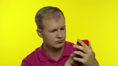 Young-caucasian-man-posing-in-pink-t-shirt.-Handsome-guy-using-mobile-phone-and-win-something
