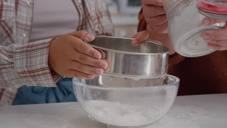 Closeup-of-grandchild-strain-flour-ingredient-in-kitchen-bowl-preparing-homemade-cookie-dough