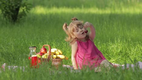 Weekend-at-picnic.-Lovely-caucasian-child-girl-on-green-grass-meadow-eating-merry,-cherry