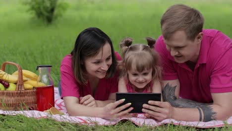 Family-weekend-picnic.-Daughter-child-girl-with-mother-and-father-play-online-games-on-tablet