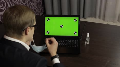 Man-removes-medical-mask,-takes-sanitizer-and-use-near-laptop-with-green-screen