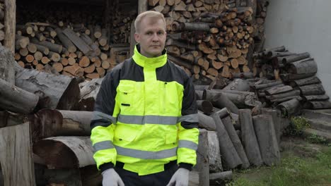 Lumberjack-in-reflective-jacket.-Man-woodcutter-show-thumbs-up.-Sawn-logs,-firewood-background