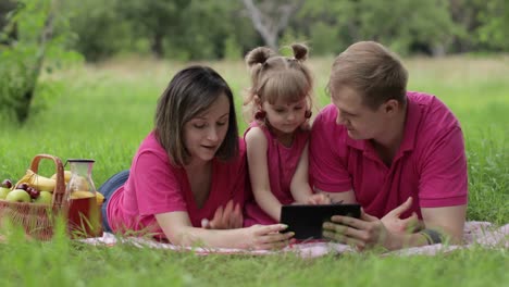 Family-weekend-picnic.-Daughter-child-girl-with-mother-and-father-browsing-on-internet-on-tablet