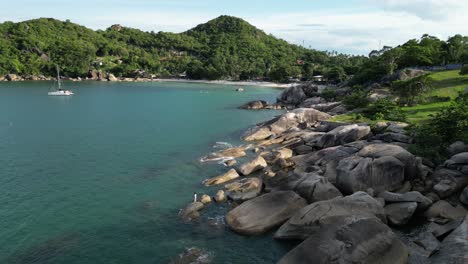 Static-shot-of-a-rocky-beach-in-the-Koh-Samui-island-groups-with-still-water-and-shore-and-boat-docked-nearby