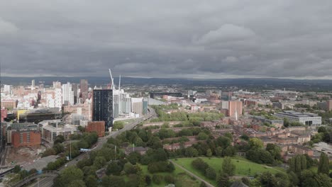 Aerial-view-flying-across-Deansgate-square-parkland-and-skyscrapers-on-overcast-Manchester-city-landscape