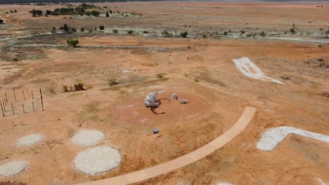 Vista-Aérea-De-Una-Extraña-Estatua-De-Dinosaurio-Cerca-De-Un-Pequeño-Pueblo-En-El-Interior-De-Australia