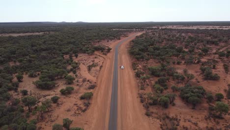 Drohne-Steigt-über-Eine-Landstraße-Und-Ein-Weißes-Geparktes-Auto,-Umgeben-Von-Roter-Erde-Im-Australischen-Outback