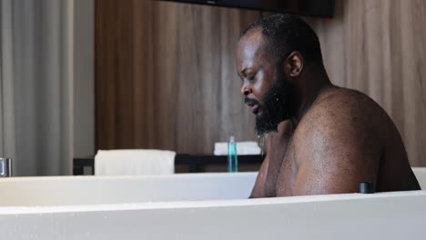 Ein-Afroamerikanischer-Mann-Badet-In-Einer-Badewanne-In-Seinem-Hotelzimmer,-Während-Das-Fensterlicht-Seine-Haut-Berührt