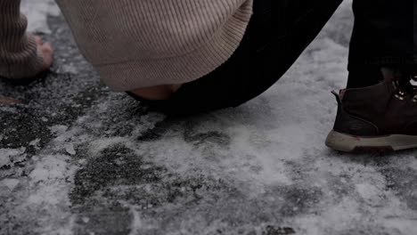 Person-slips-on-ice-and-falls-to-ground-in-slow-motion,-hurt-ankle-and-hand-closeup