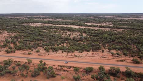 Drohne-Fliegt-über-Ein-Geparktes-Weißes-Auto-Und-Eine-Landstraße-In-Richtung-Eines-Kesselgrundstücks-Im-Australischen-Outback