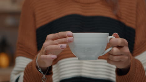 Close-up-of-tea-cup-held-by-young-woman-at-home