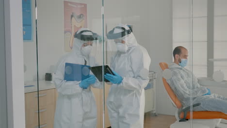 Team-of-dentists-with-ppe-suits-holding-tablet-for-teeth-consultation