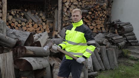 Lumberjack-in-reflective-jacket.-Man-woodcutter-hold-huge-axe.-Sawn-logs,-firewood-background