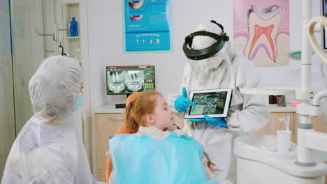 Dentist-in-protective-equipment-showing-on-tablet-dental-x-ray-reviewing-it
