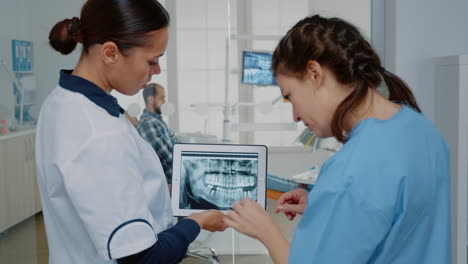 Dentist-and-nurse-analyzing-teeth-radiography-on-tablet