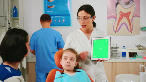 Stomatologist-woman-looking-at-green-screen-tablet-while-speaking-with-mother