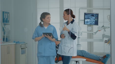 Professioneller-Zahnarzt,-Der-Mit-Der-Krankenschwester-Spricht-Und-Auf-Ein-Digitales-Tablet-Schaut