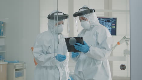 Orthodontists-wearing-protection-suits-looking-at-tablet