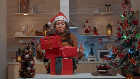 Woman-with-santa-hat-carrying-gifts-in-decorated-kitchen