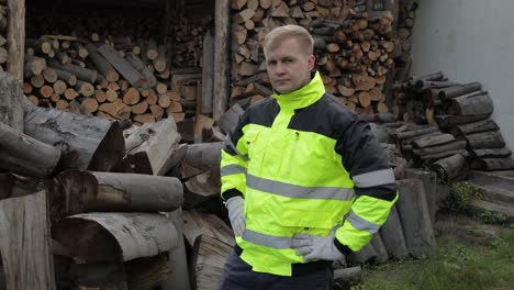 Lumberjack-in-reflective-jacket.-Man-woodcutter-show-thumb-up.-Sawn-logs,-firewood-background