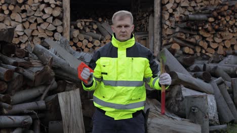 Lumberjack-in-reflective-jacket.-Man-woodcutter-holds-small-axe-and-saw-on-his-hands.-Firewood