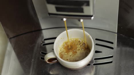 Espresso-shot-pouring-out-from-coffee-machine-in-small-white-and-brown-cup.-Close-up-footage