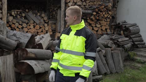 Lumberjack-in-reflective-jacket.-Man-woodcutter-show-thumb-up.-Sawn-logs,-firewood-background
