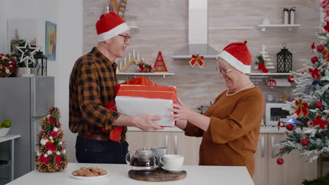 Älteres-Paar-Mit-Weihnachtsmannmütze-Teilt-Weihnachtsgeschenkverpackung-Mit-Schleife