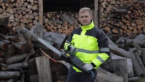 Lumberjack-in-reflective-jacket.-Man-woodcutter-with-electric-chainsaw.-Show-ok-sign.-Sawmill
