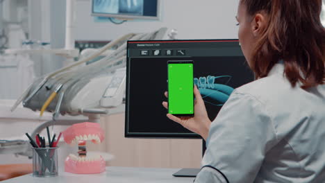 Dentist-vertically-holding-smartphone-with-green-screen