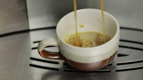 Espresso-shot-pouring-out-from-coffee-machine-in-small-white-and-brown-cup.-Close-up-footage