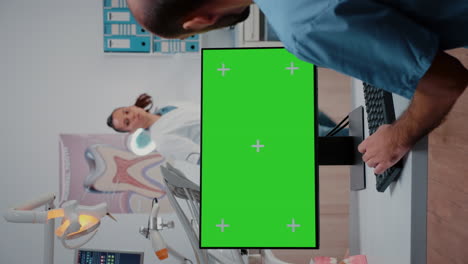 Vertical-video:-Assistant-looking-at-horizontal-green-screen-on-computer