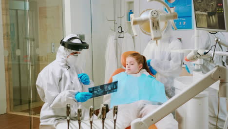 Dentist-with-coverall-holding-mouth-x-ray-image-child-patient-talking