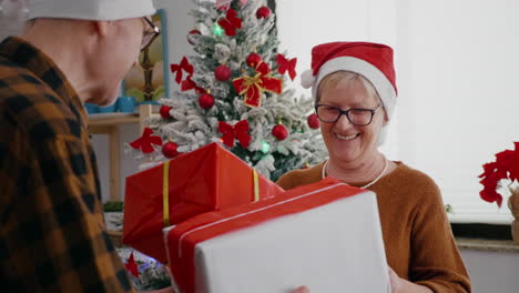 Feliz-Pareja-De-Ancianos-Disfrutando-De-Navidad-Compartiendo-Envoltorio-De-Regalo-Presente-En-La-Cocina-Decorada-De-Navidad