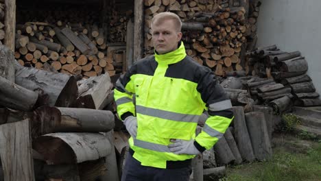 Lumberjack-in-reflective-jacket.-Man-woodcutter-show-ok-sign.-Sawn-logs,-firewood-background