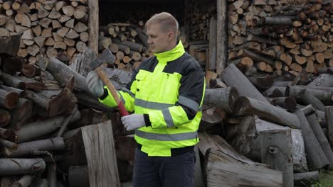 Lumberjack-in-reflective-jacket.-Man-woodcutter-with-small-axe.-Sawn-logs,-firewood-background