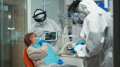 Stomatologe-Im-Schutzanzug-überprüft-Die-Röntgenaufnahme-Des-Zahns-Mithilfe-Eines-Tablets