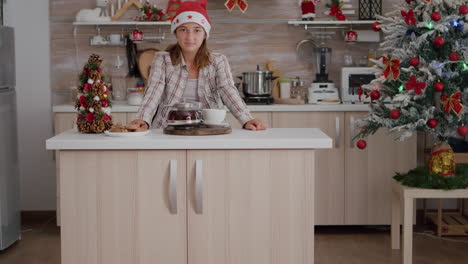 Portrait-of-girl-wearing-santa-hat-looking-into-camera-standing-at-table-in-xmas-decorated-kitchen